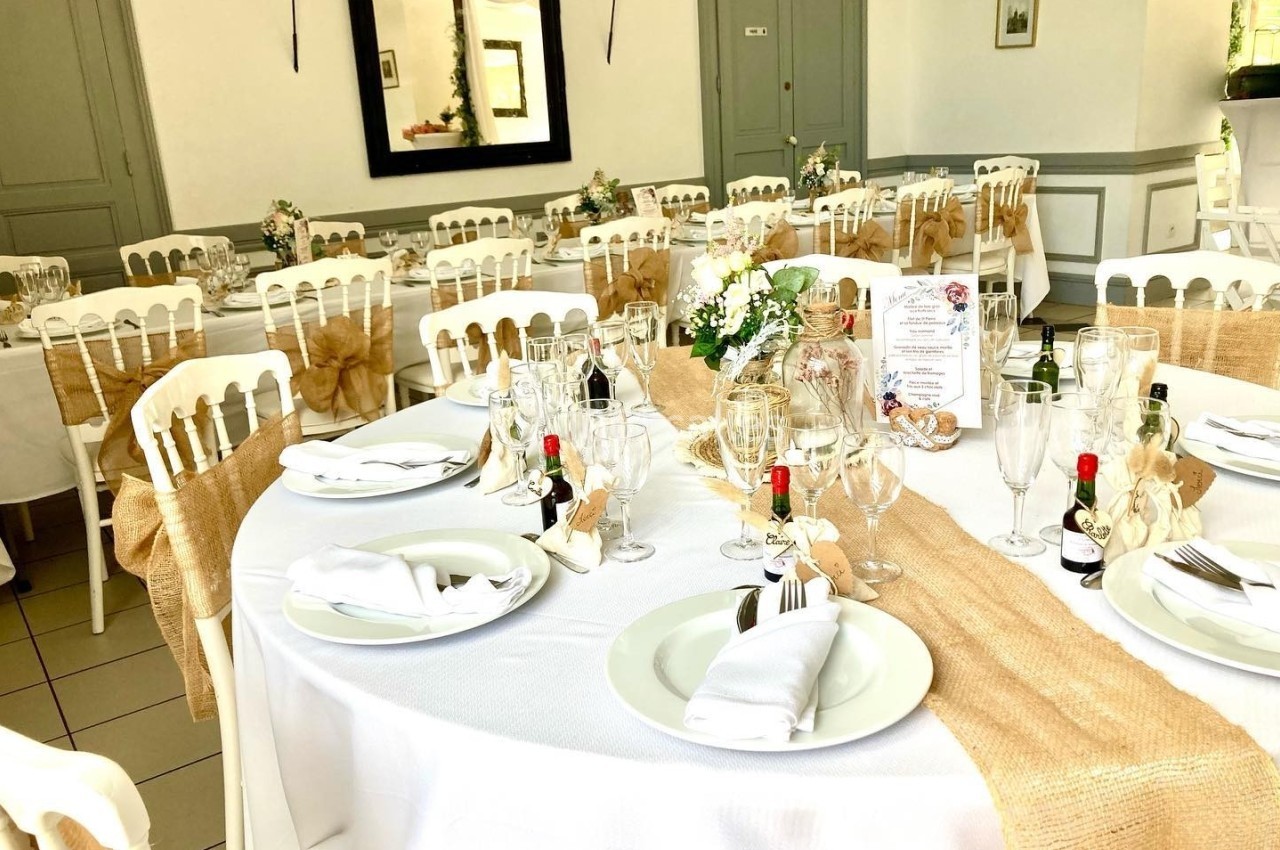Salle de réception décorée avec des tables rondes dressées, nappes blanches et chemins de table en toile de jute.