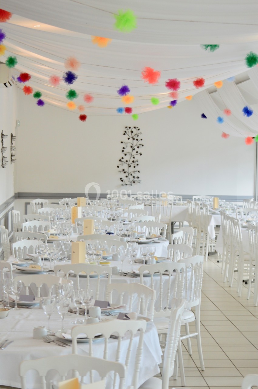 Salle de réception décorée avec des tables dressées et des guirlandes colorées suspendues au plafond.