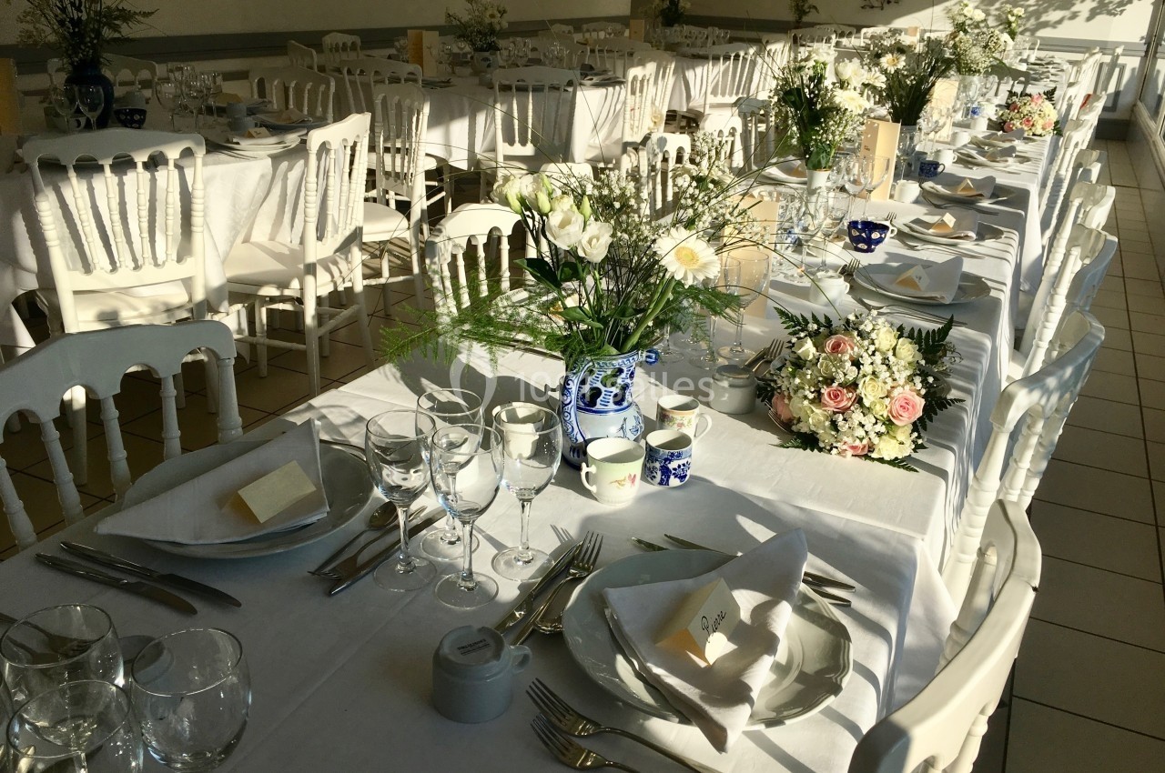 Tables de réception élégamment dressées avec nappes blanches, vaisselle, verres et bouquets de fleurs.