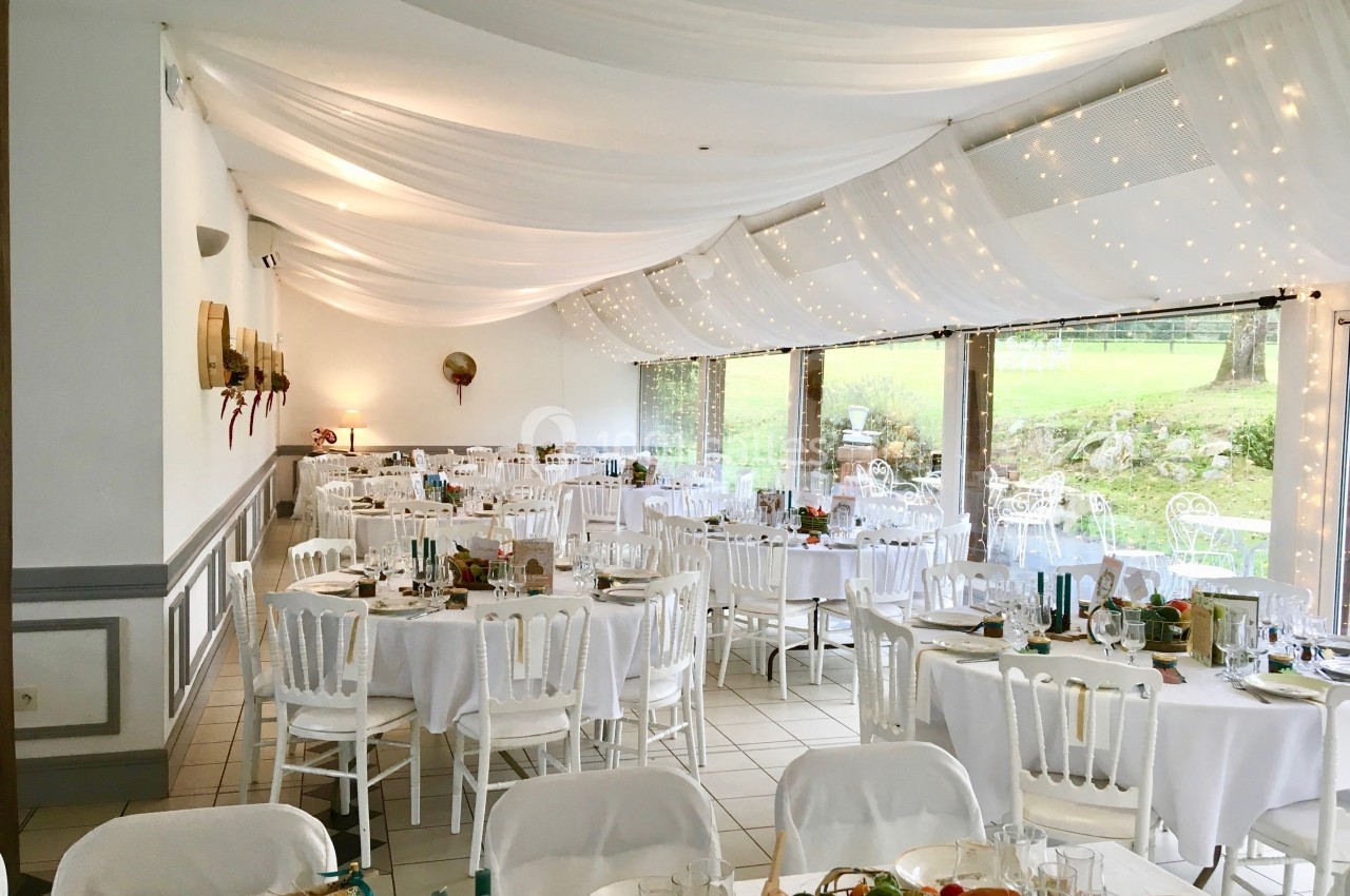 Salle de réception décorée avec des tables rondes dressées, des chaises blanches et un plafond drapé de voilages lumineux.