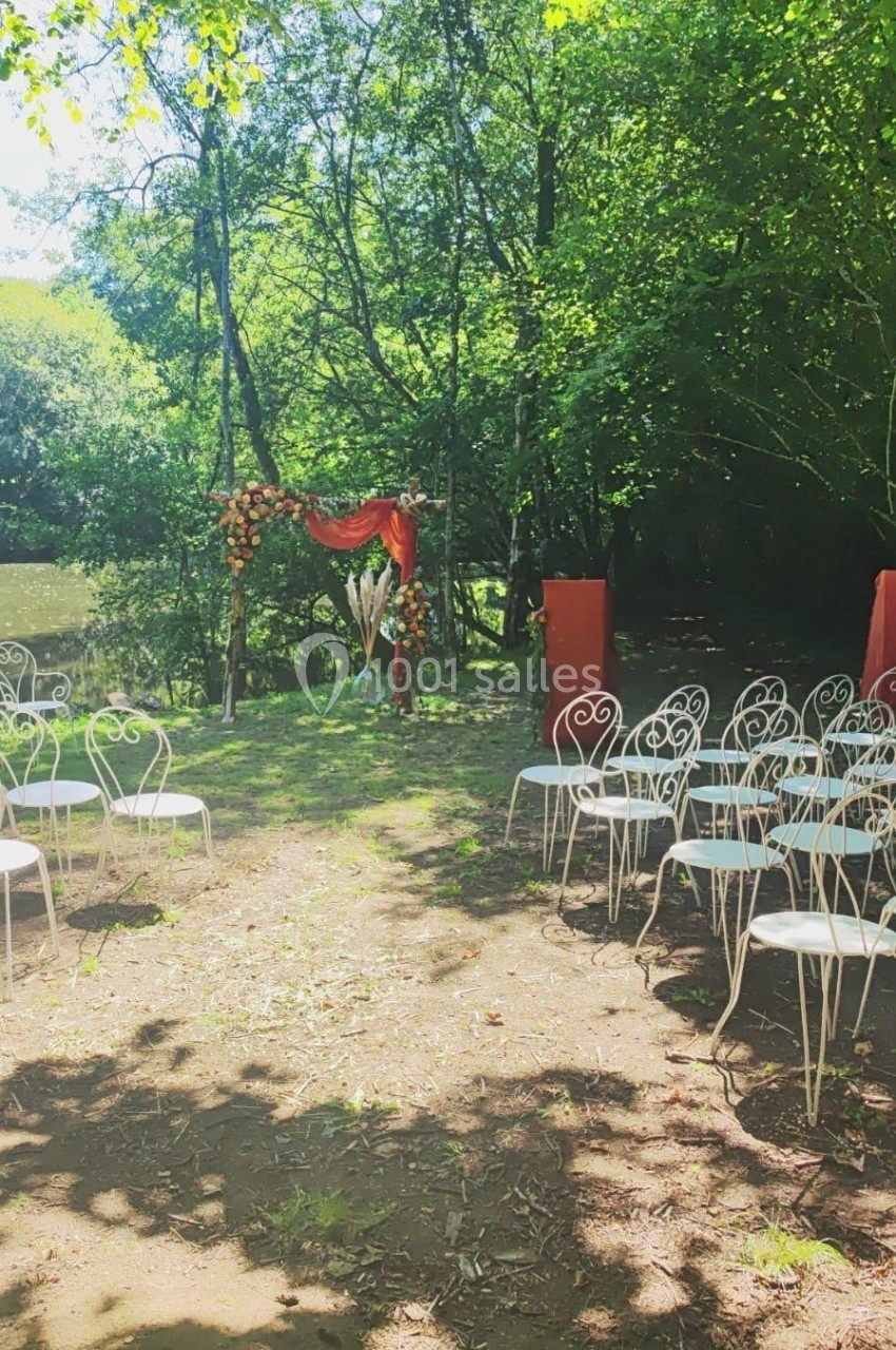 Chaises blanches disposées en extérieur devant une arche fleurie, entourées d'arbres et de verdure.