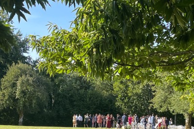 Groupe de personnes rassemblées dans un jardin verdoyant par une journée ensoleillée.