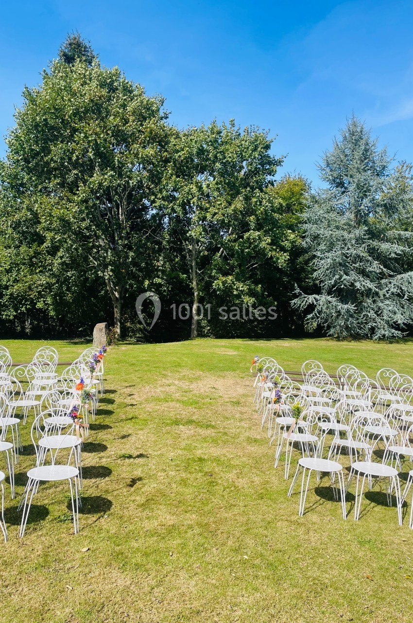 Chaises blanches alignées en extérieur, formant une allée centrale sur une pelouse, entourée d'arbres.