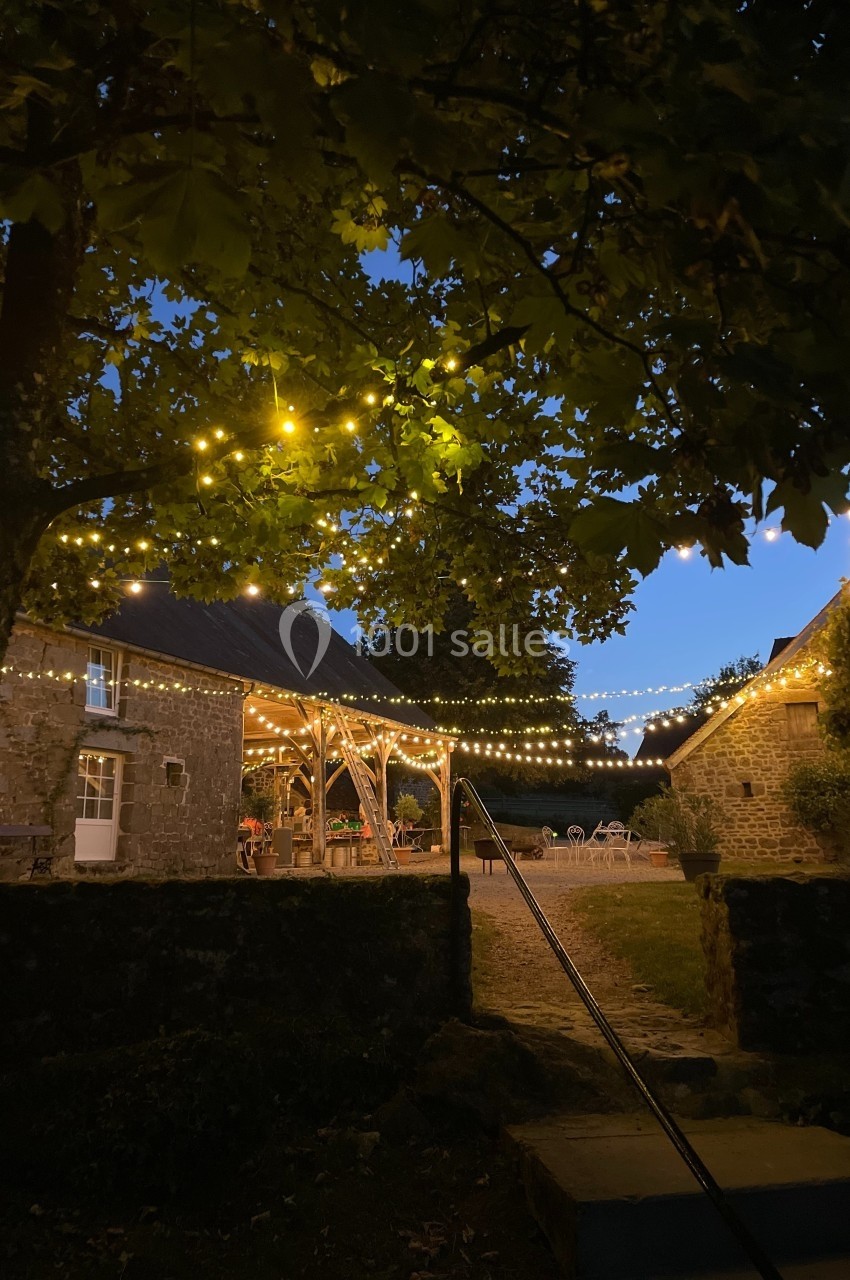 Cour extérieure illuminée par des guirlandes lumineuses, entourée de bâtiments en pierre au crépuscule.