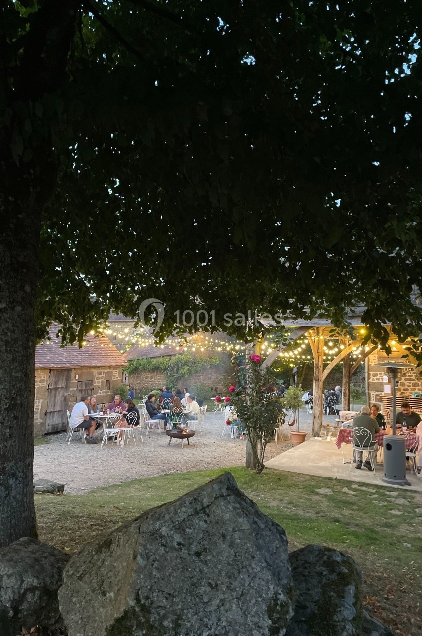 Dîner en plein air sous des guirlandes lumineuses, près d'un arbre et de rochers, dans une ambiance champêtre.