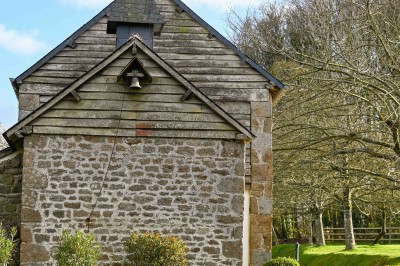 Façade en pierre d'une maison avec toit en tuiles, vue partiellement à travers des branches fleuries au premier plan.