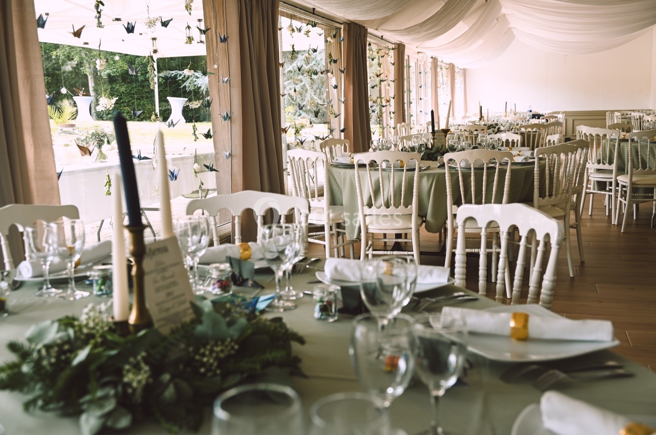 Salle de réception décorée avec des tables dressées, nappes vertes, chaises blanches et guirlandes de papier suspendues.