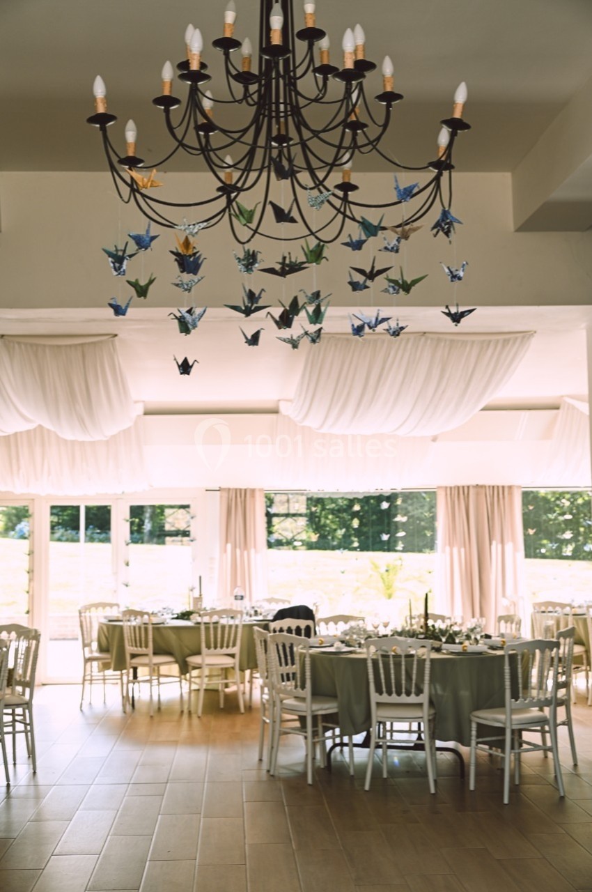 Salle de réception lumineuse décorée de grues en origami suspendues et de tables dressées avec nappes vertes.