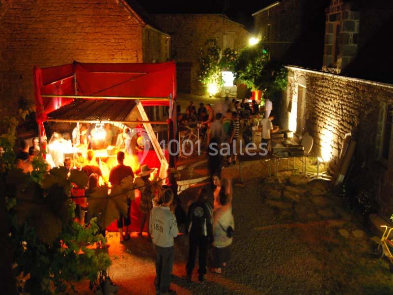 Un marché nocturne animé avec des stands éclairés et des visiteurs dans une cour en pierre.