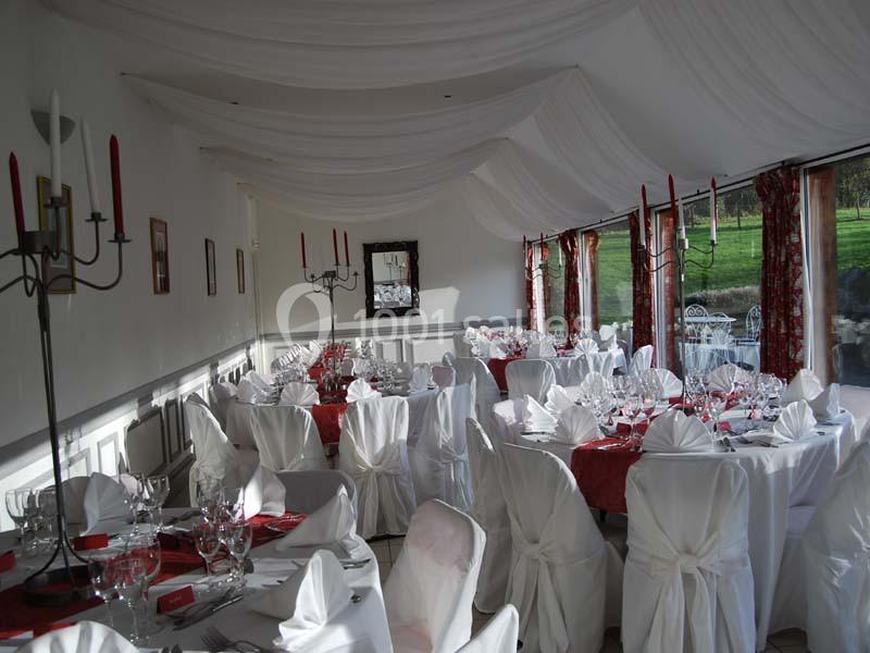 Salle de réception élégante avec nappes blanches, chandeliers et grandes baies vitrées donnant sur un jardin.