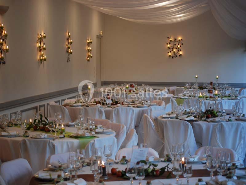 Salle de réception décorée avec des tables rondes, nappes blanches, chandeliers et arrangements floraux.