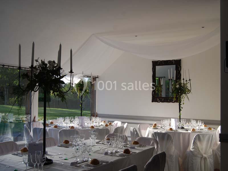 Salle de réception lumineuse avec tables dressées, nappes blanches, chandeliers et vue sur un jardin verdoyant.