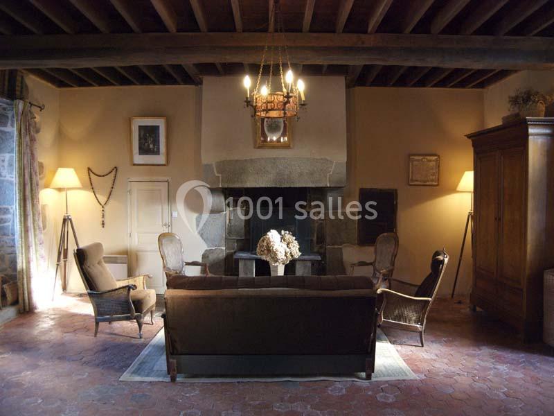 Salon rustique avec poutres apparentes, cheminée en pierre, mobilier ancien et éclairage chaleureux.