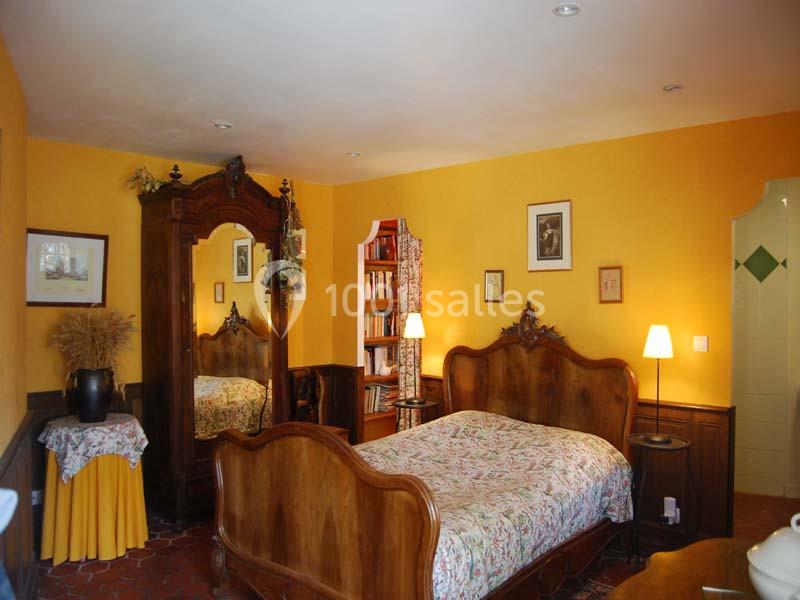 Chambre avec lit double, armoire en bois, murs jaunes, lampes de chevet et accès partiel à une salle de bain.