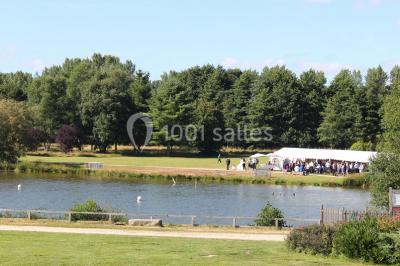 Une personne joue au tennis sur un court extérieur entouré d'arbres, sous un ciel dégagé.