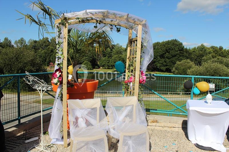 Arche de mariage décorée de fleurs et de voiles, entourée de chaises blanches, en extérieur par une journée ensoleillée.