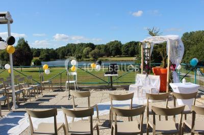 Une personne joue au tennis sur un court extérieur entouré d'arbres, sous un ciel dégagé.