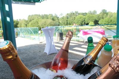 Une personne joue au tennis sur un court extérieur entouré d'arbres, sous un ciel dégagé.