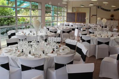 Une personne joue au tennis sur un court extérieur entouré d'arbres, sous un ciel dégagé.