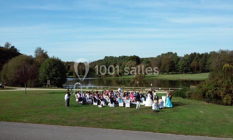 Cérémonie en plein air avec des invités assis sur une pelouse, près d'un lac entouré d'arbres.