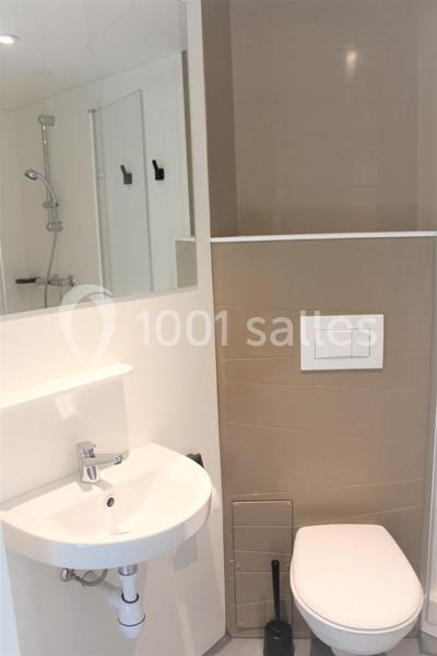 Salle de bain compacte avec lavabo, miroir, toilettes suspendues et douche avec paroi vitrée en arrière-plan.