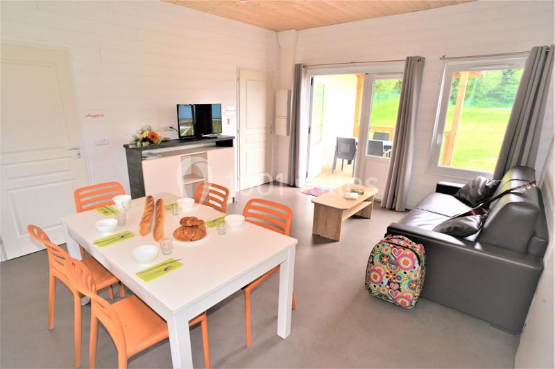 Salle de séjour lumineuse avec table dressée, canapé, télévision, et vue sur une terrasse donnant sur un espace vert.