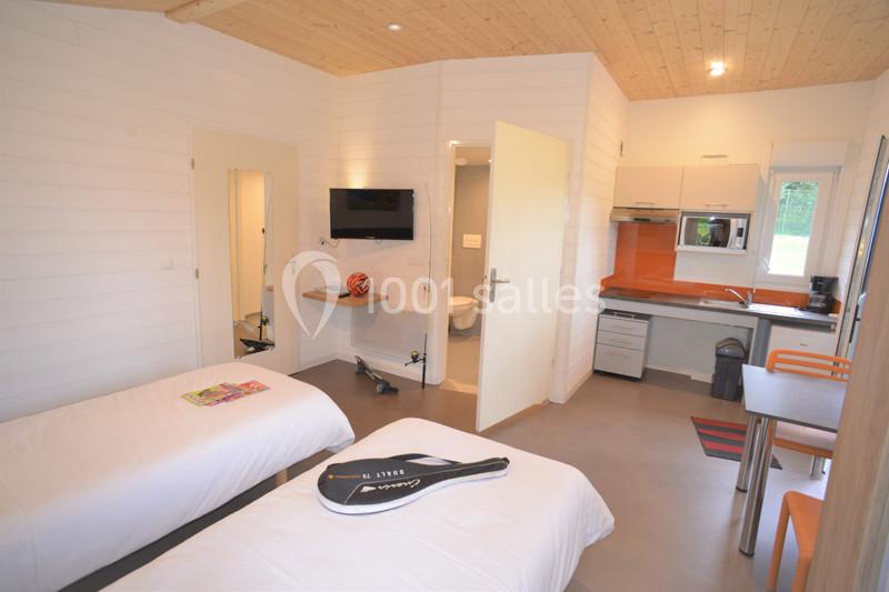 Chambre lumineuse avec deux lits simples, kitchenette équipée, table à manger et salle de bain attenante.