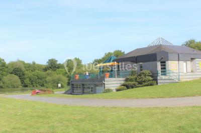 Une personne joue au tennis sur un court extérieur entouré d'arbres, sous un ciel dégagé.