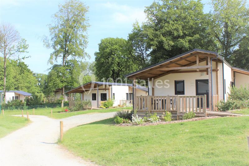 Chalets en bois avec terrasses, situés dans un cadre verdoyant et entourés d'arbres.
