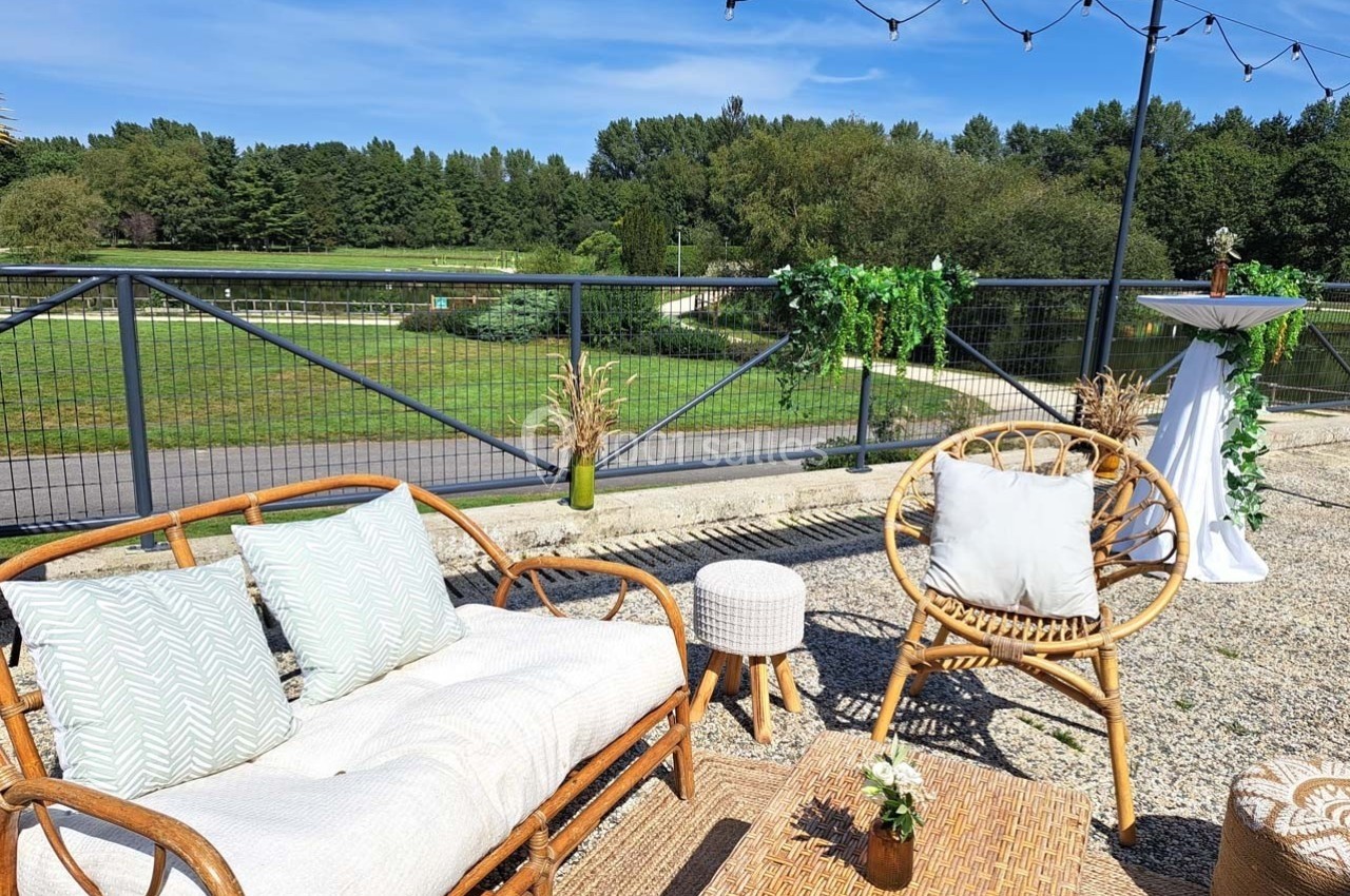 Mobilier en rotin disposé en extérieur avec vue sur un espace vert, décoré de plantes et guirlandes lumineuses.