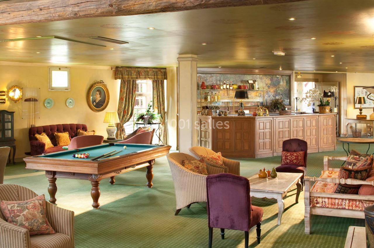 Salle chaleureuse avec table de billard, fauteuils confortables, bar en bois et décoration élégante.