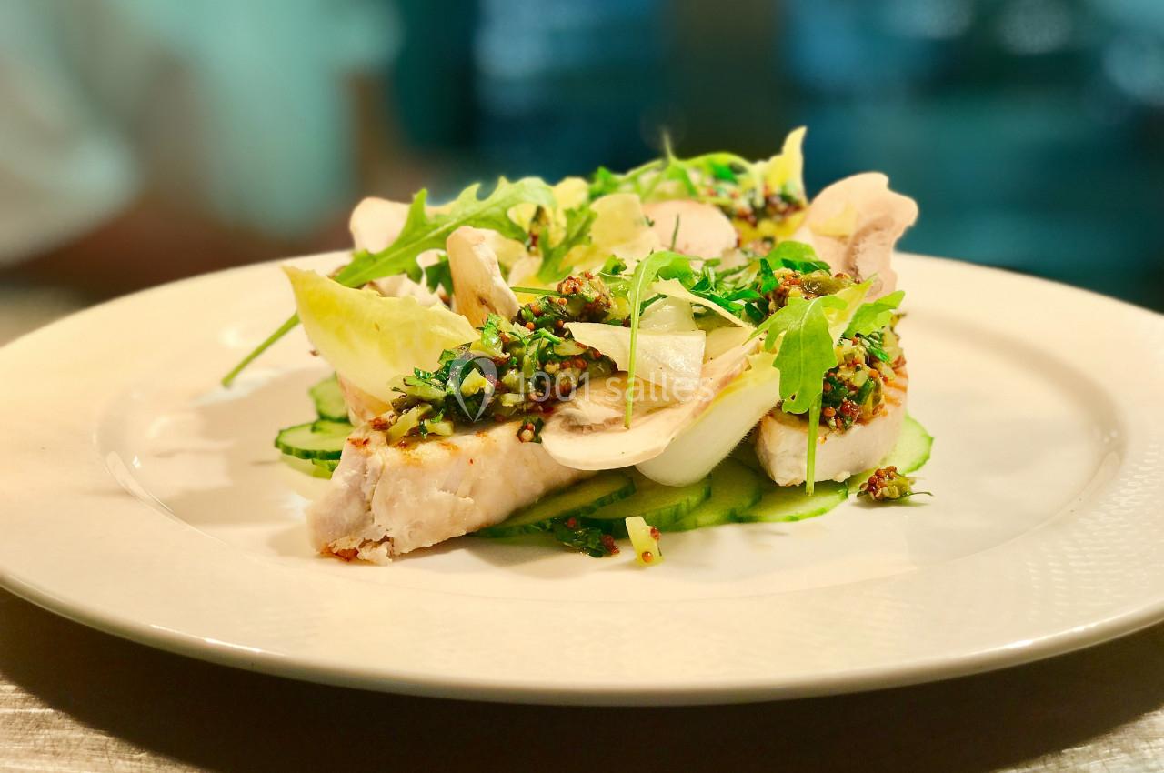 Assiette de poisson blanc garni de légumes verts, herbes fraîches et sauce aux graines, servie sur une table lumineuse.