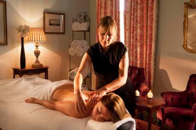 Une femme reçoit un massage sur une table dans une pièce chaleureuse avec des rideaux, des bougies et une lumière tamisée.