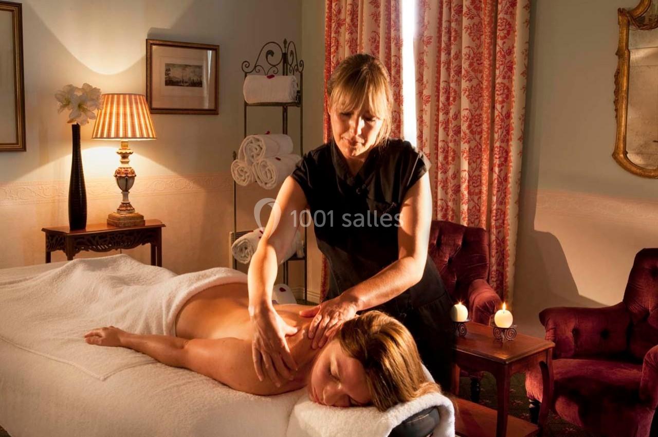 Une femme reçoit un massage sur une table dans une pièce chaleureuse avec des rideaux, des bougies et une lumière tamisée.