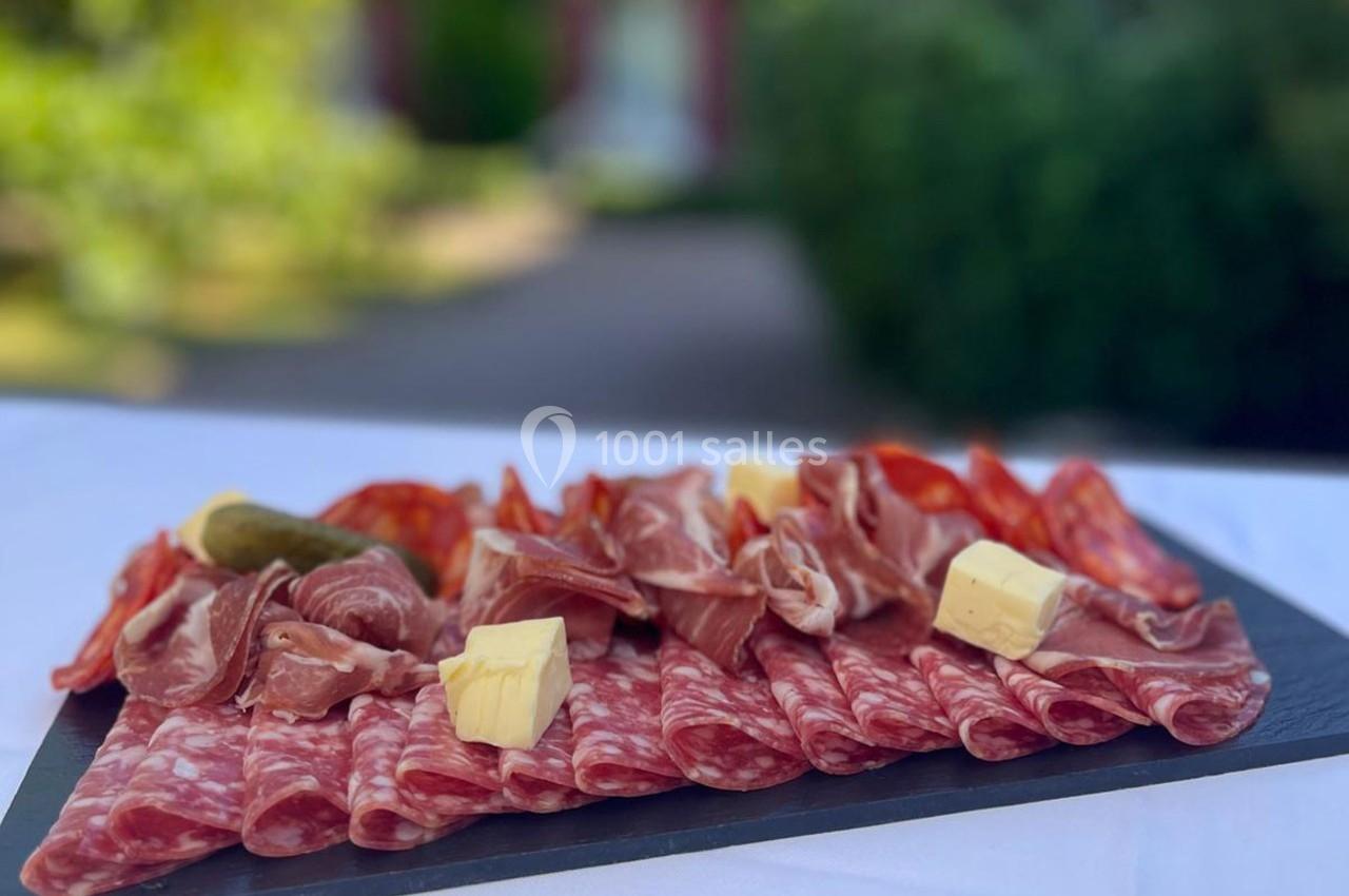 Plateau de charcuterie variée avec tranches de saucisson, jambon, fromage et cornichon, présenté sur une table en extérieur.