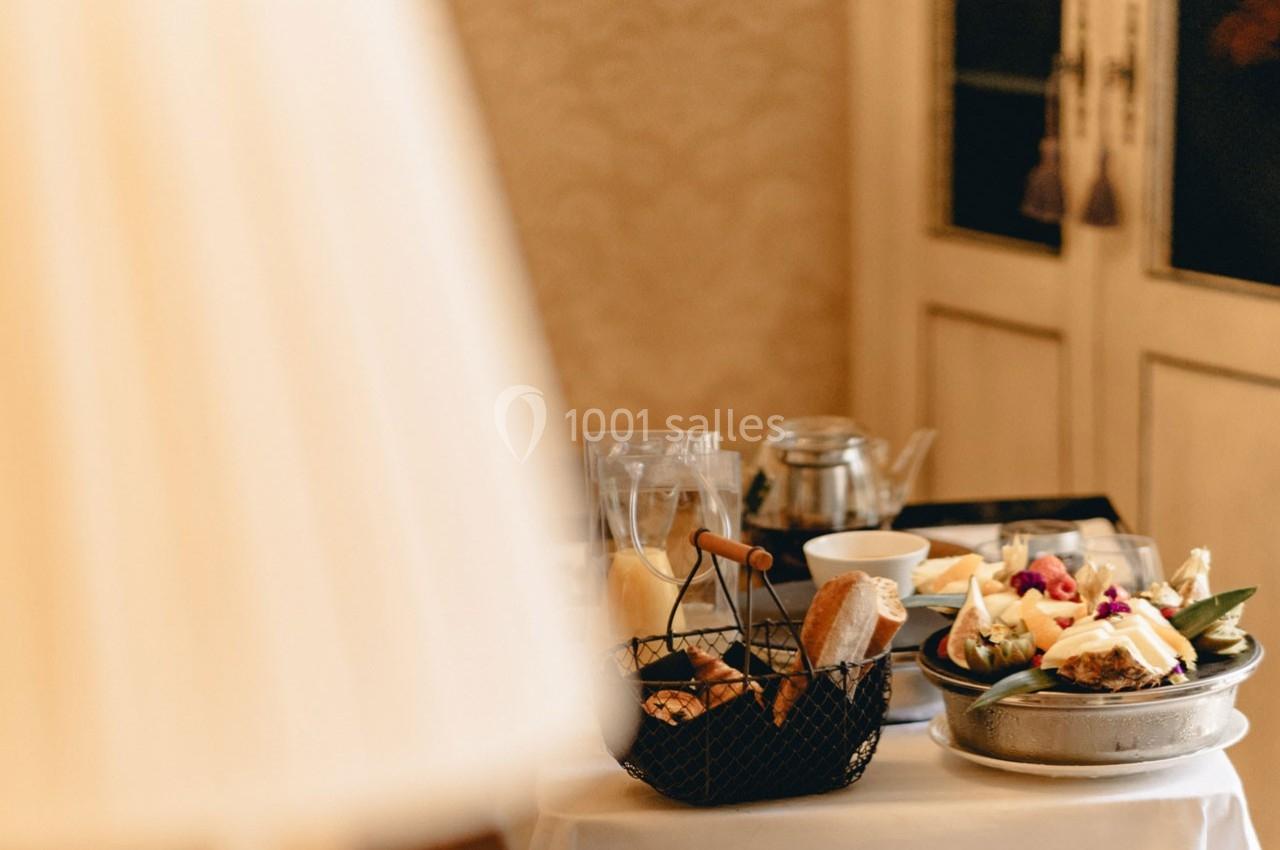 Petit-déjeuner servi sur une table avec viennoiseries, fruits, théière et assiettes, dans un décor chaleureux.