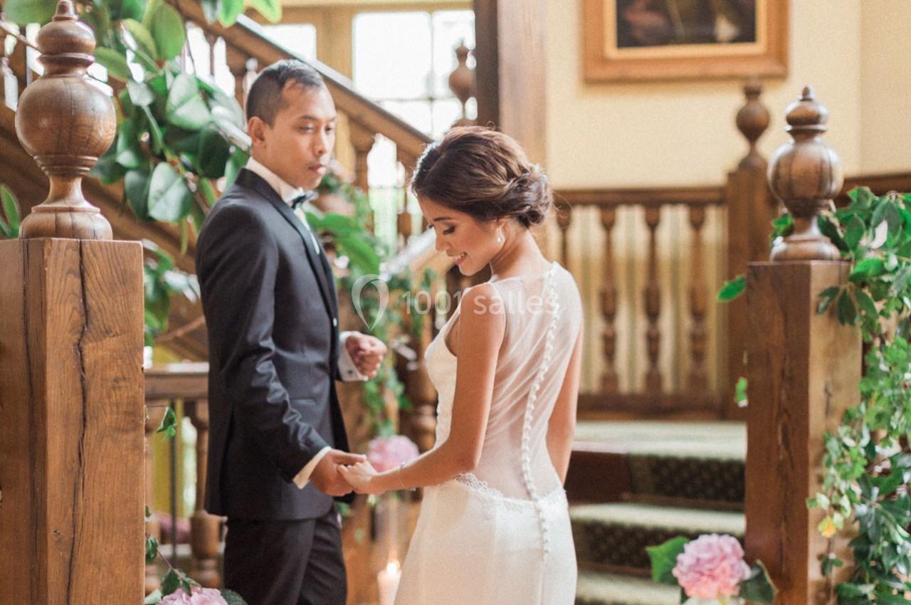 Un couple en tenue de mariage se tient la main devant un escalier décoré de plantes et de fleurs.