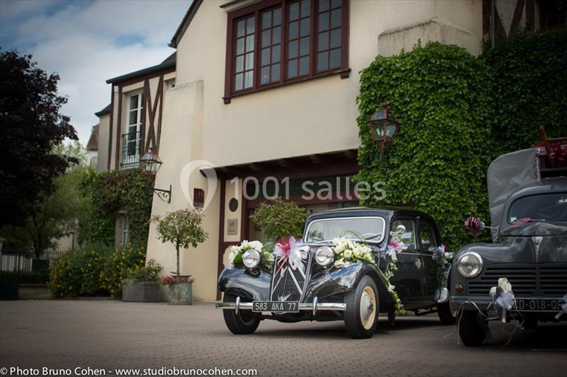 Voiture ancienne décorée de fleurs garée devant une maison avec façade en lierre et colombages.