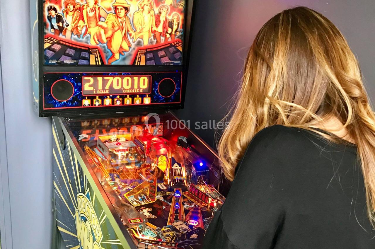 Une femme joue à un flipper rétro dans une pièce aux murs sombres.