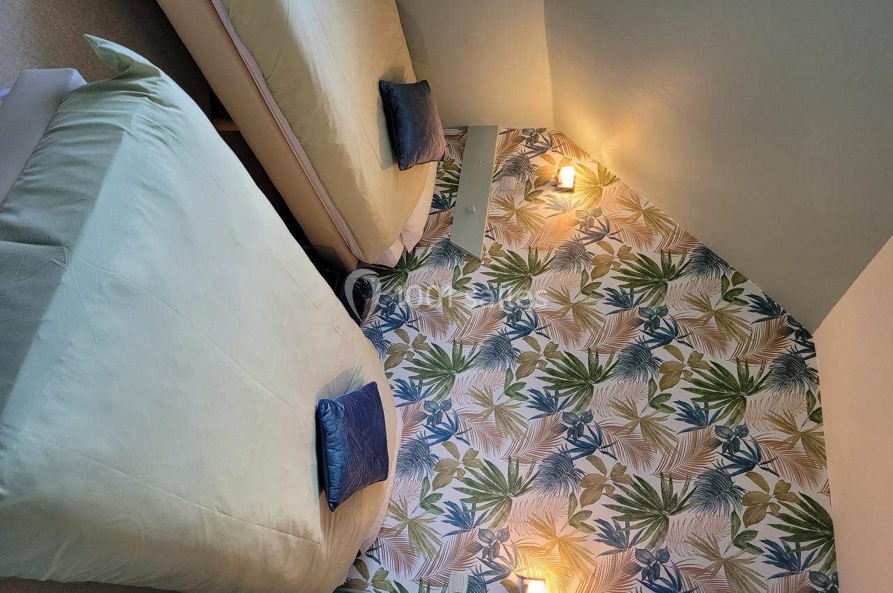 Deux lits simples avec coussins bleus dans une chambre aux murs décorés d'un papier peint à motifs végétaux.