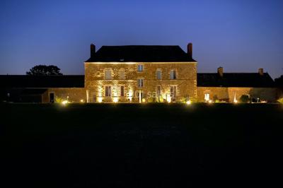 Façade d'une grande maison en pierre éclairée la nuit, entourée d'un jardin sombre et d'annexes.