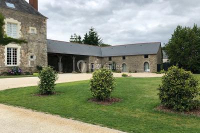 Façade d'une grande maison en pierre éclairée la nuit, entourée d'un jardin sombre et d'annexes.