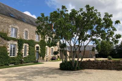 Façade d'une grande maison en pierre éclairée la nuit, entourée d'un jardin sombre et d'annexes.