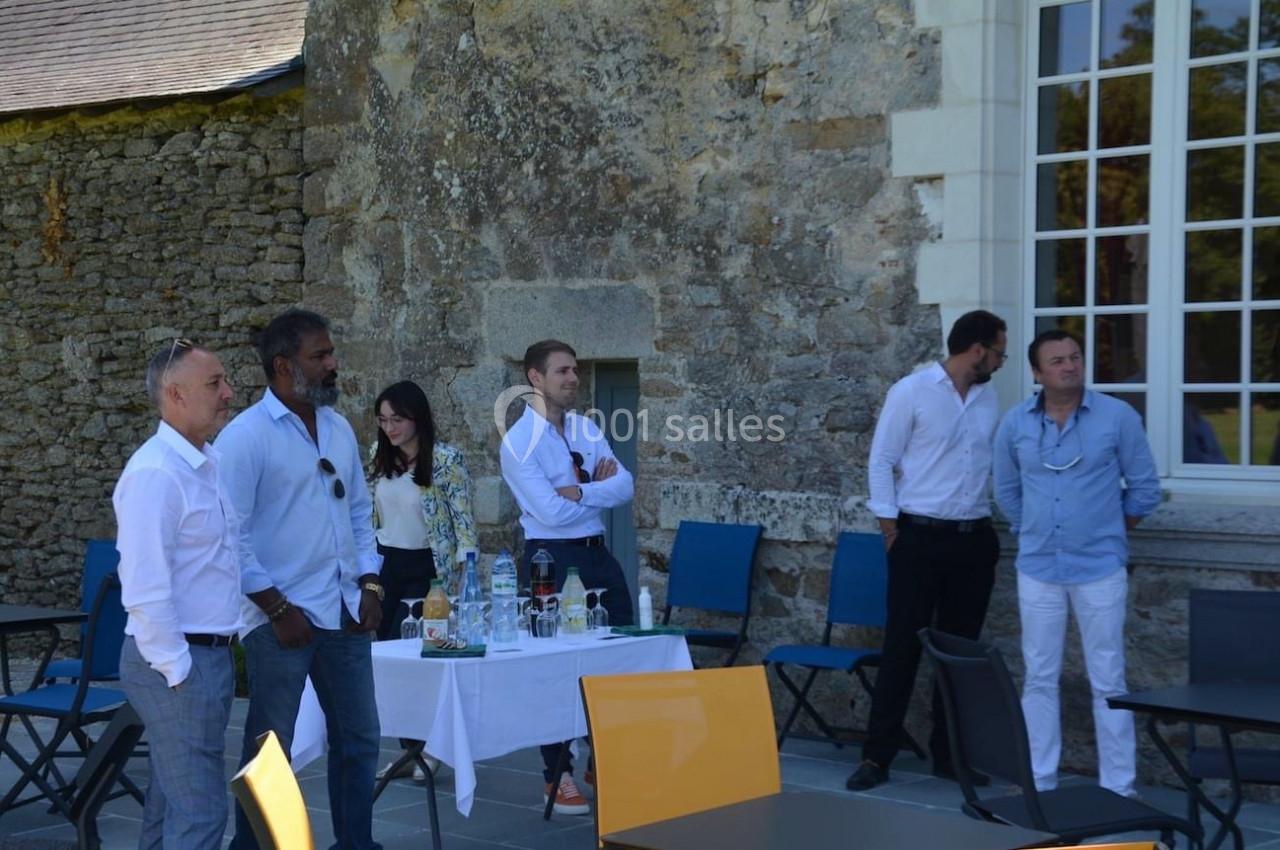 Des personnes debout près d'une table avec des boissons, devant un mur en pierre et une grande fenêtre.