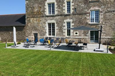 Façade d'une grande maison en pierre éclairée la nuit, entourée d'un jardin sombre et d'annexes.