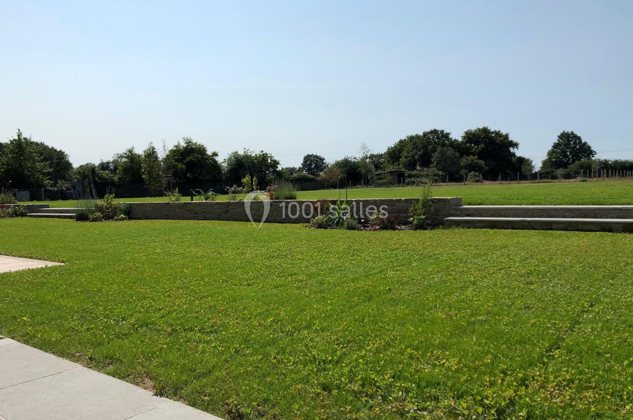 Pelouse verte bien entretenue avec quelques parterres de plantes, bordée de murets en pierre et d'arbres à l'arrière-plan.