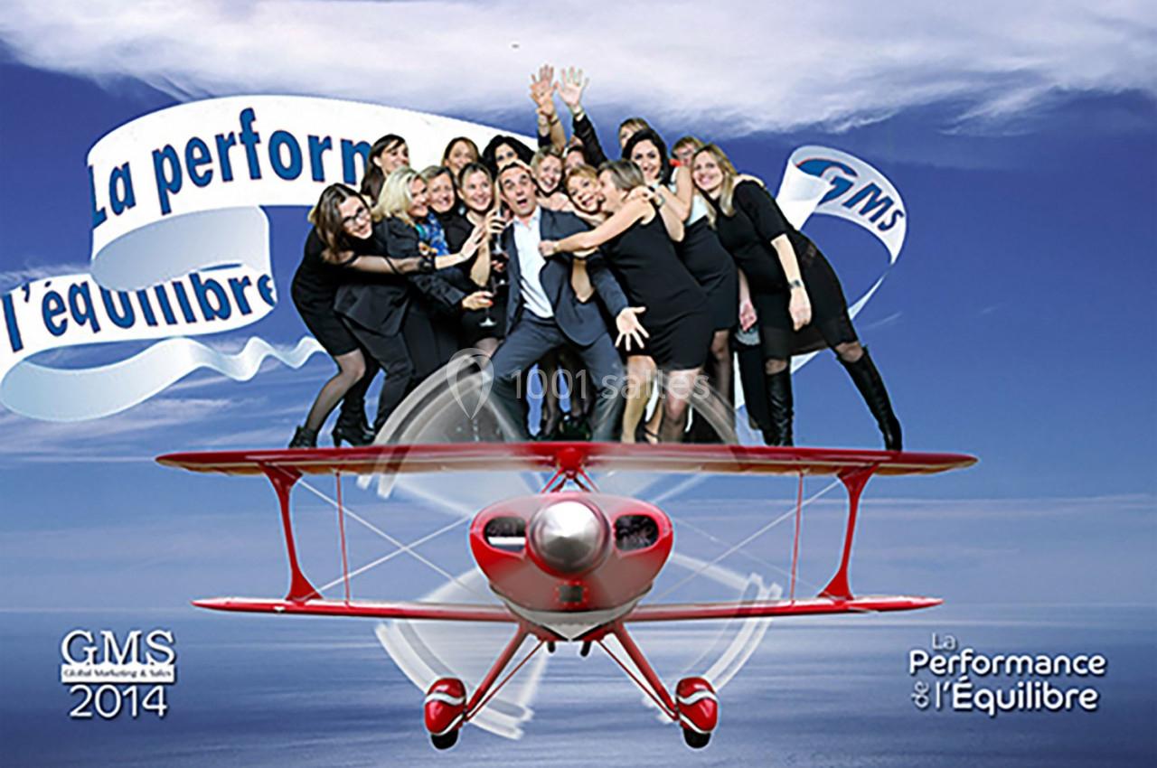 Un groupe de personnes souriantes posant sur une illustration d'avion rouge, avec des banderoles en arrière-plan.