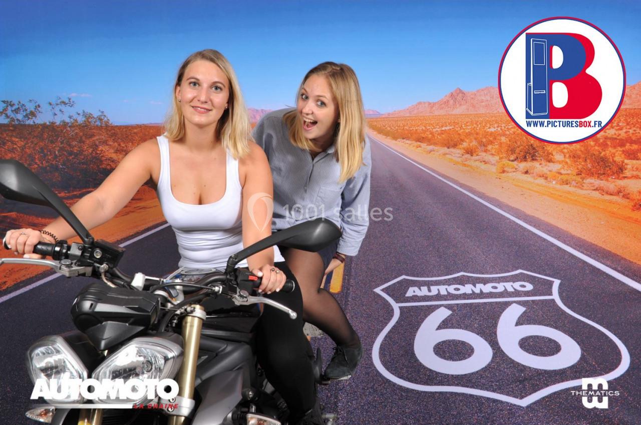 Deux femmes posent devant un décor de route désertique avec une moto et un logo ’AutomoTo 66’.