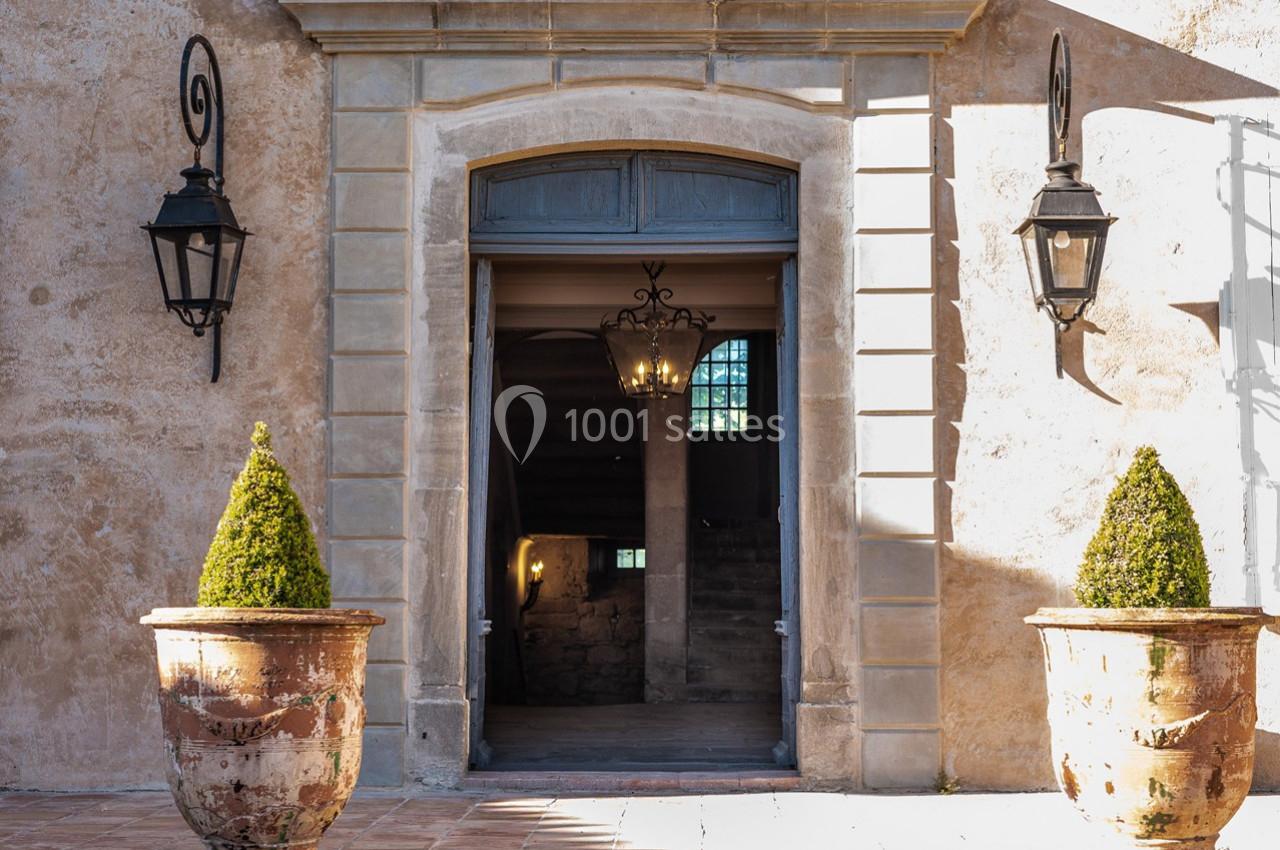 Entrée d'un bâtiment ancien avec porte ouverte, deux lanternes murales et deux pots en terre cuite contenant des arbustes…