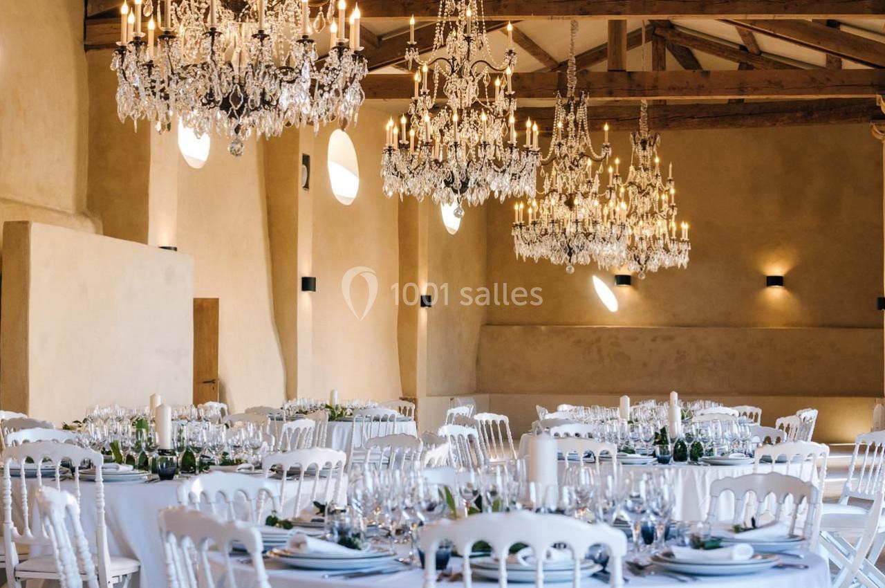 Salle de réception élégante avec tables dressées, chaises blanches et lustres en cristal suspendus au plafond en bois.